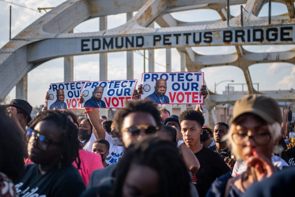 People march across the Edmund Pettus Bridge with placards bearing the image of the late U.S. Rep. John Lewis